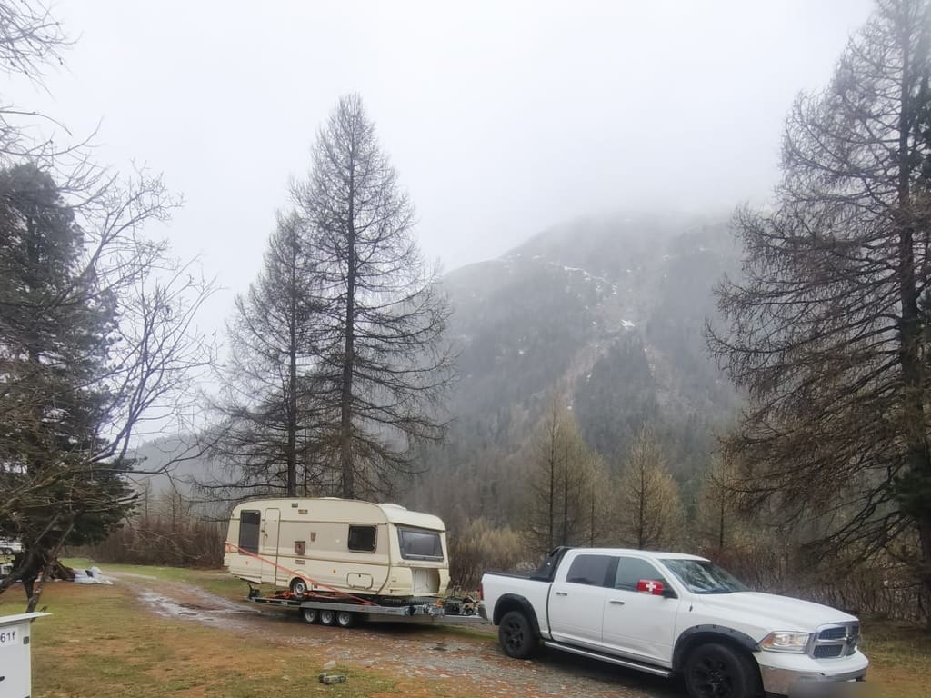 Wohnwagen gesichert auf dem Anhänger von SWISS Abschleppservice vor Bergkulisse